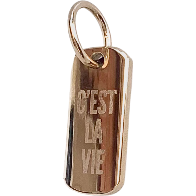 A gold-colored polished brass pendant with the phrase 'C'est la vie' engraved on it, featuring a lobster clasp fastening.