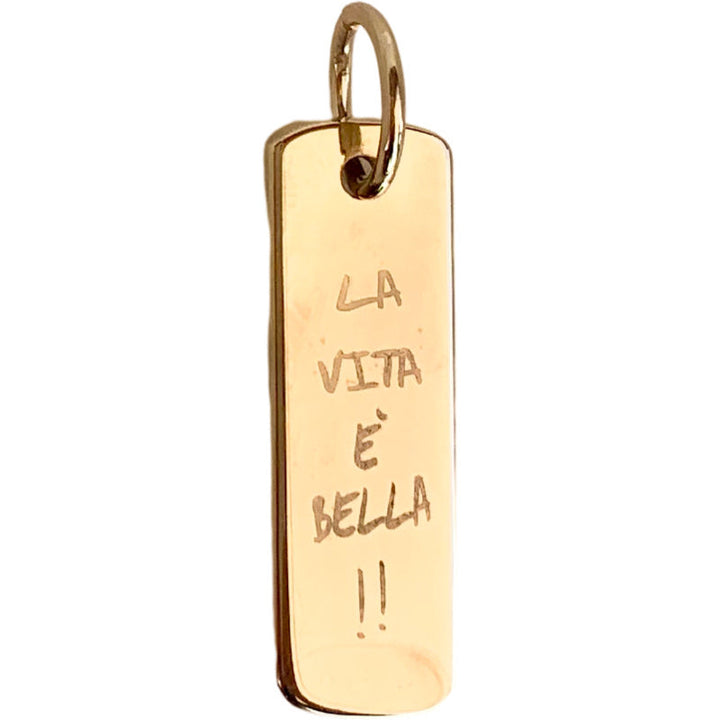A gold-plated brass pendant with the inscription 'LA VITA E³ BELLA' in a cursive script.
