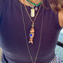Person wearing a purple top with layered necklaces, including a fish-shaped pendant.