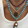 Necklace with turquoise beads and fish pendant on a white tank top
