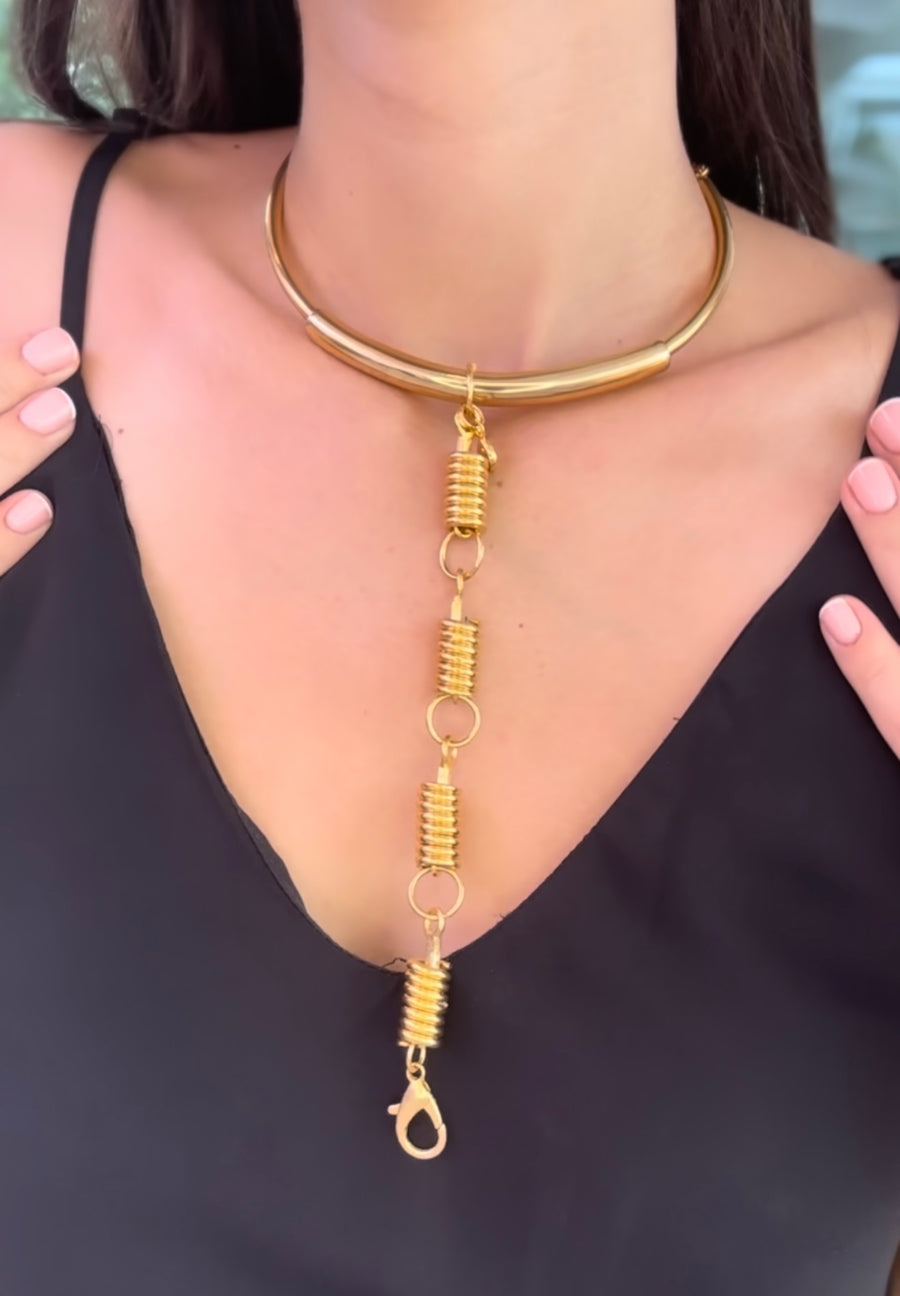 Gold necklace with a unique design worn by a person against a black background